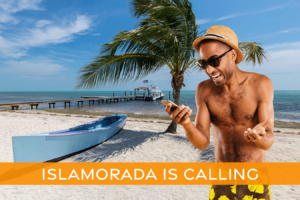 Man in bathing suit looking at his phone and smiling while standing on the beach in Islamorada.